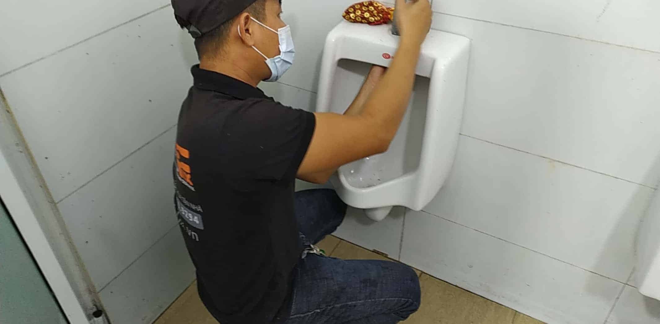 Bồn tiểu nam cảm ứng màu trắng được lắp đặt hoàn chỉnh, sạch sẽ trên tường gạch men màu xám.