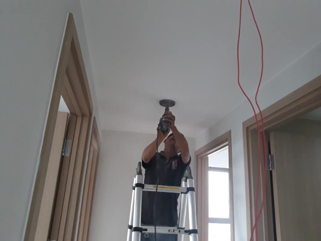 Thợ điện đang dùng máy khoét lỗ chuyên dụng để cắt trần thạch cao lắp đèn